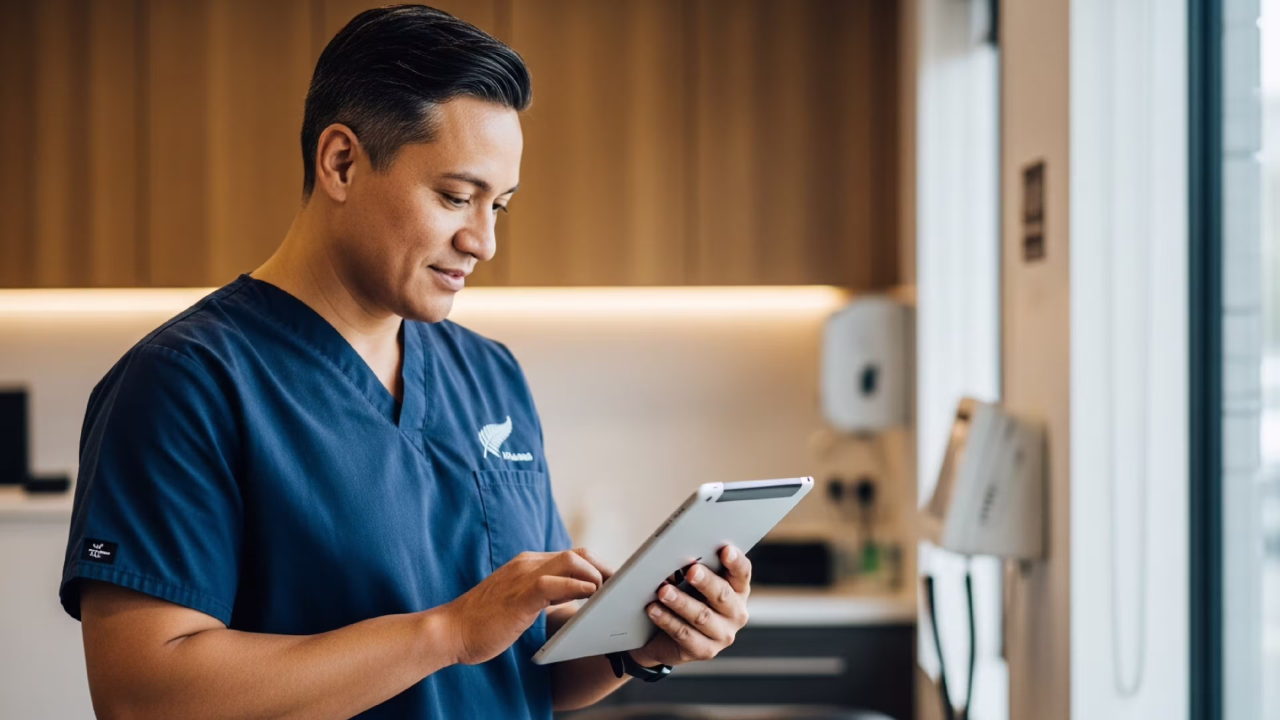 NZ healthcare professional using practice management software on a tablet in a clinical setting